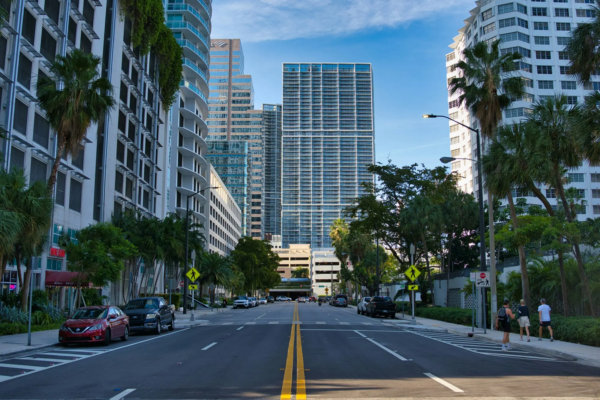A palm-lined boulevard with residential towers on either side, seen from street level